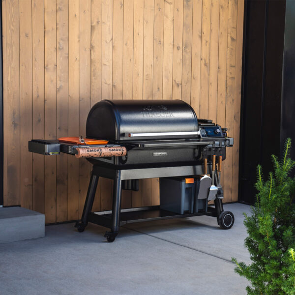 Traeger Ironwood XL @ Fourth Element - Black, Barrel Shaped BBQ outside on concrete pad in front of wood panelled wall.